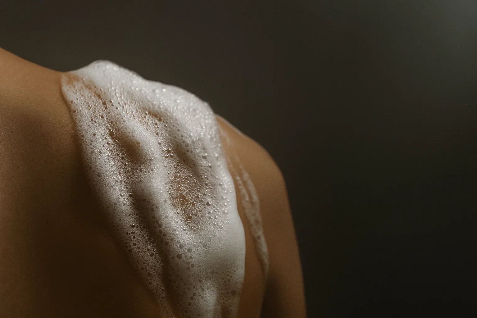 Foamy soap lather on a person's shoulder against a dark background