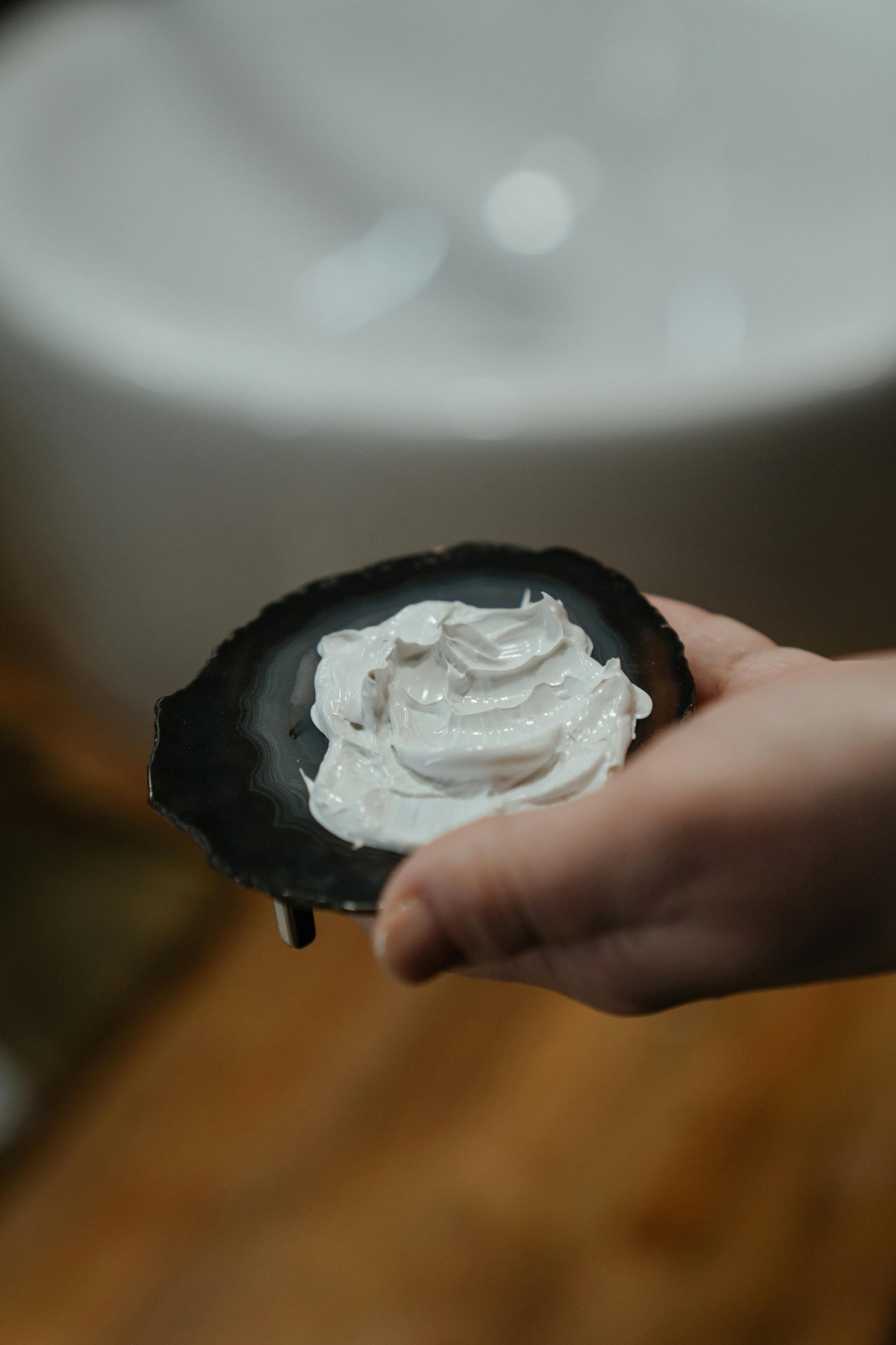 Hand holding a dark tray with white paste on a blurred background