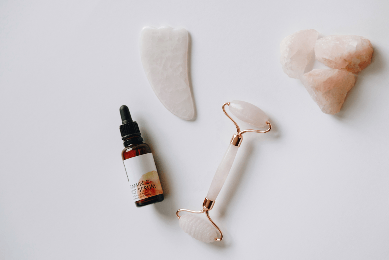 Skincare tools including a dropper bottle, roller, and stones on a light background